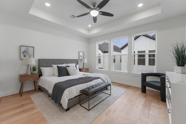 bedroom featuring ceiling fan, a raised ceiling, and light hardwood / wood-style floors