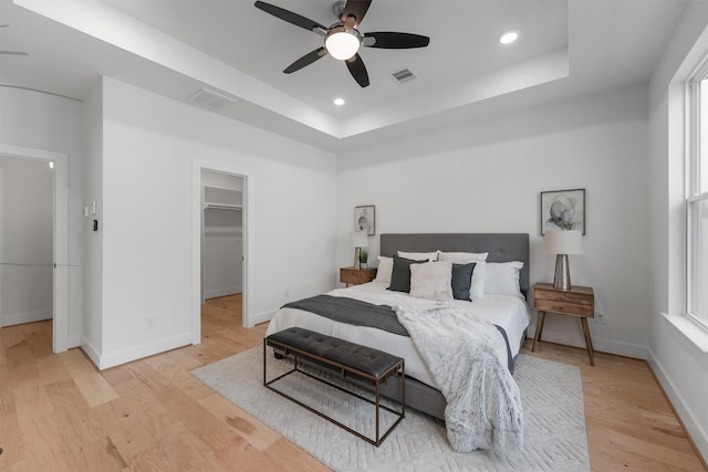 bedroom with ceiling fan, a tray ceiling, a closet, and a walk in closet