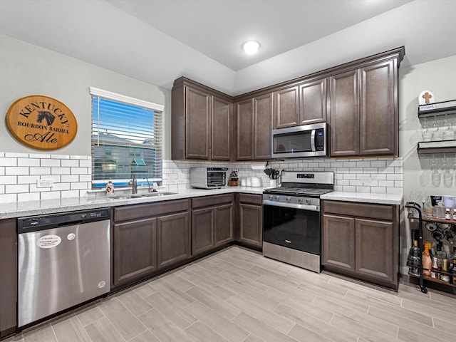 kitchen featuring appliances with stainless steel finishes, dark brown cabinets, light stone countertops, sink, and light hardwood / wood-style flooring