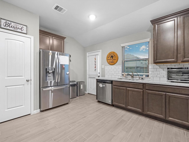 kitchen with appliances with stainless steel finishes, dark brown cabinetry, backsplash, and sink