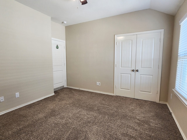 unfurnished bedroom with ceiling fan, dark colored carpet, a closet, and lofted ceiling