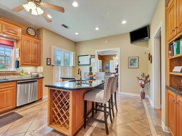 kitchen featuring dark stone countertops, an island with sink, light tile patterned floors, ceiling fan, and stainless steel dishwasher