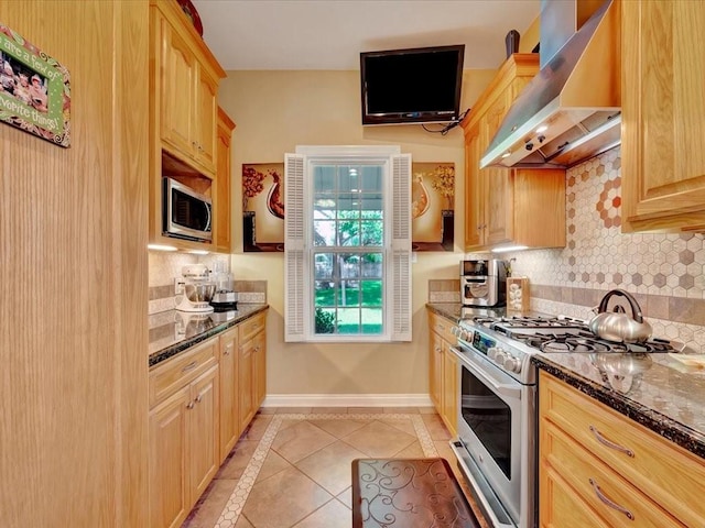 kitchen with appliances with stainless steel finishes, light tile patterned floors, dark stone counters, light brown cabinets, and extractor fan