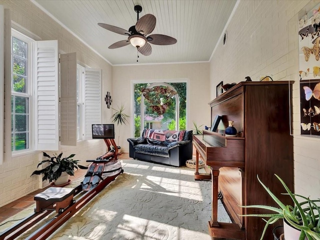 living area featuring ceiling fan, ornamental molding, and brick wall