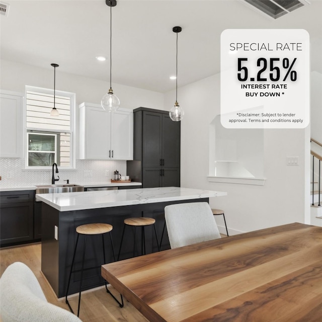 kitchen featuring decorative backsplash, a kitchen island, light wood finished floors, and a sink