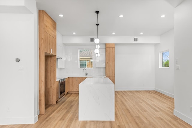 kitchen featuring sink, light hardwood / wood-style floors, range, a kitchen island, and pendant lighting