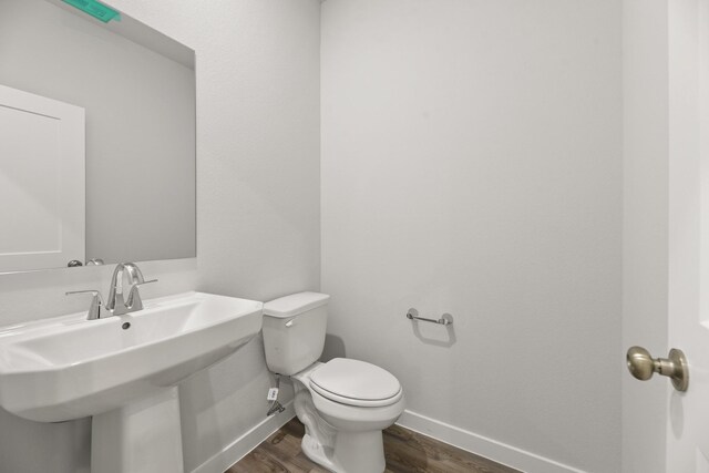 half bath with baseboards, toilet, a sink, and wood finished floors