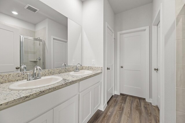 bathroom with wood finished floors, a sink, a shower stall, and visible vents