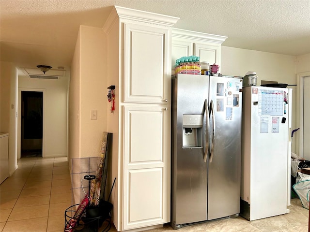 kitchen with a textured ceiling, white fridge, light tile patterned floors, stainless steel refrigerator with ice dispenser, and white cabinetry