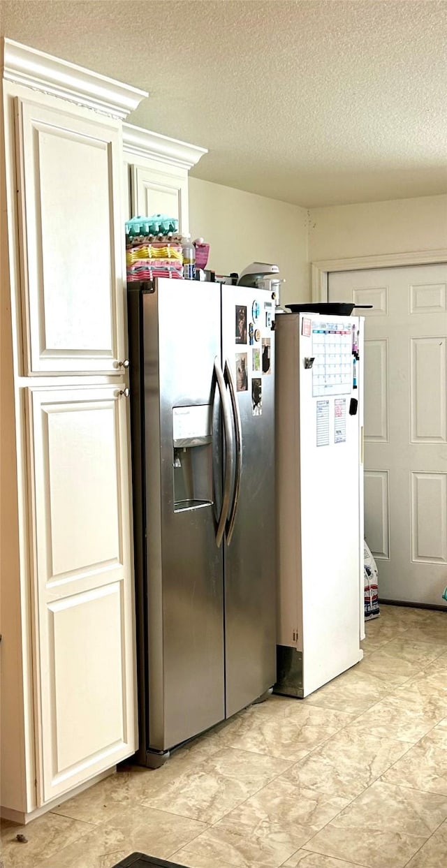 kitchen with a textured ceiling, stainless steel fridge, white fridge, and cream cabinetry