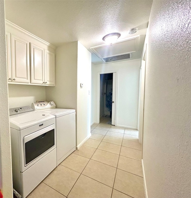 laundry area featuring a textured ceiling, washing machine and dryer, cabinets, and light tile patterned floors