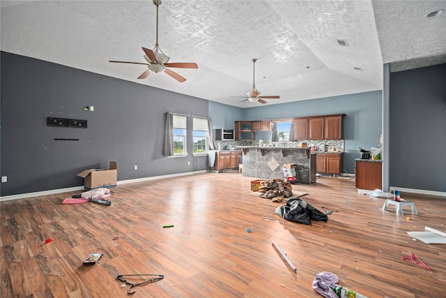 living room with ceiling fan, vaulted ceiling, a textured ceiling, and light hardwood / wood-style floors