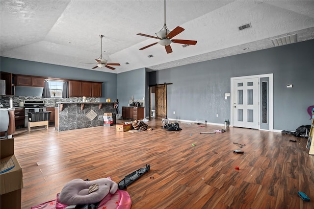 living room with wood-type flooring, vaulted ceiling, ceiling fan, a tray ceiling, and a barn door