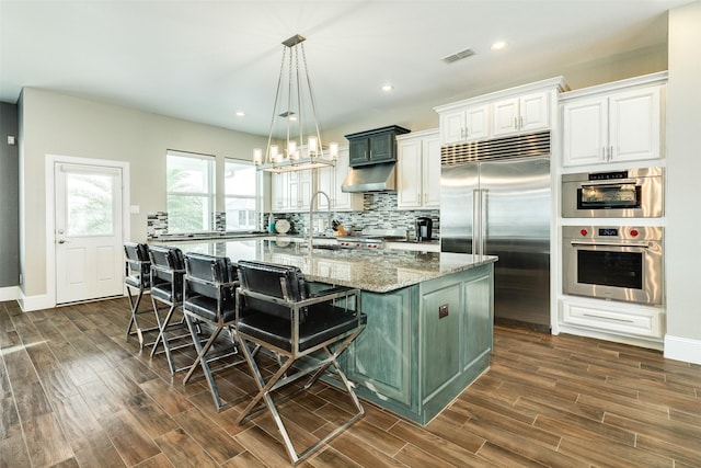 kitchen featuring a breakfast bar area, appliances with stainless steel finishes, hanging light fixtures, an island with sink, and light stone countertops