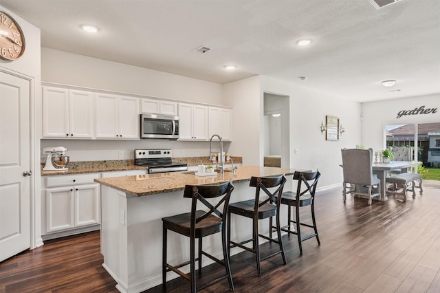 kitchen featuring a breakfast bar, appliances with stainless steel finishes, light stone countertops, dark wood finished floors, and a center island with sink