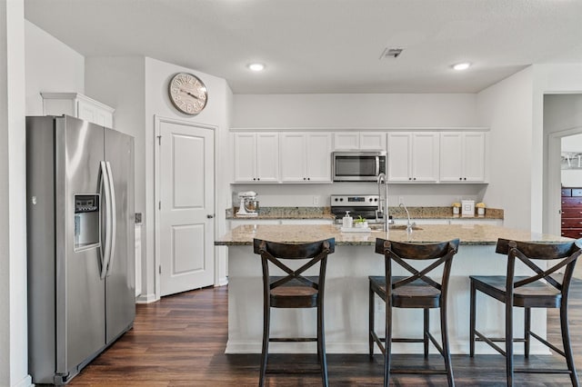 kitchen with light stone counters, dark wood finished floors, stainless steel appliances, visible vents, and white cabinets