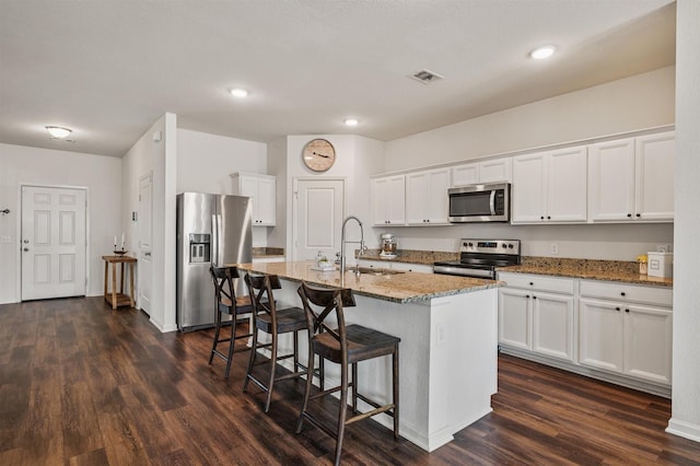 kitchen featuring light stone counters, dark wood finished floors, appliances with stainless steel finishes, a sink, and a kitchen bar