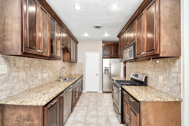 kitchen featuring light stone countertops, stainless steel appliances, tasteful backsplash, light tile patterned flooring, and sink