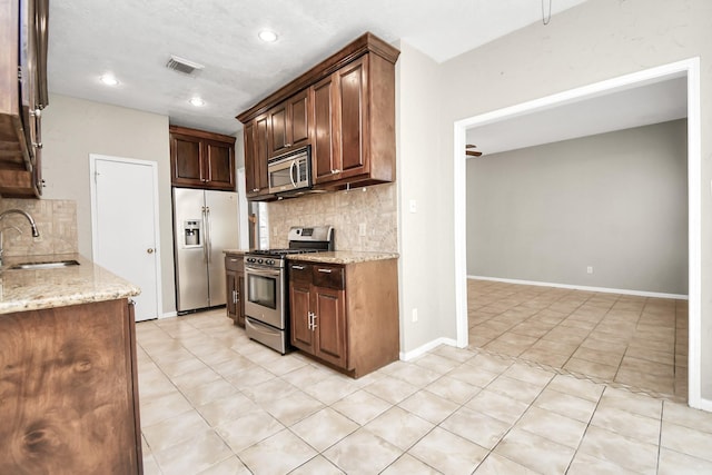 kitchen with sink, light tile patterned floors, decorative backsplash, light stone countertops, and appliances with stainless steel finishes