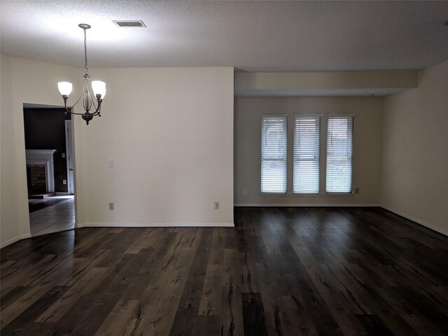 spare room with a textured ceiling, dark hardwood / wood-style floors, a chandelier, and a fireplace