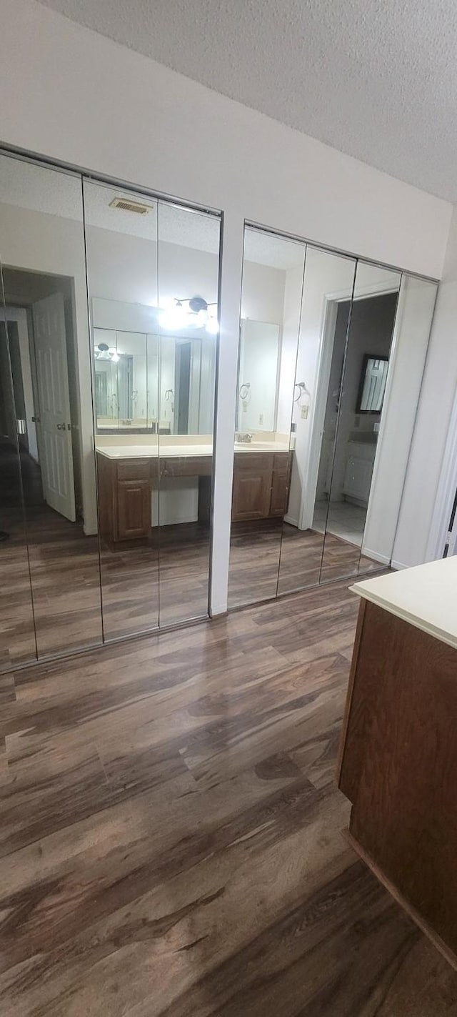 unfurnished bedroom featuring multiple closets, dark hardwood / wood-style flooring, ensuite bathroom, and a textured ceiling