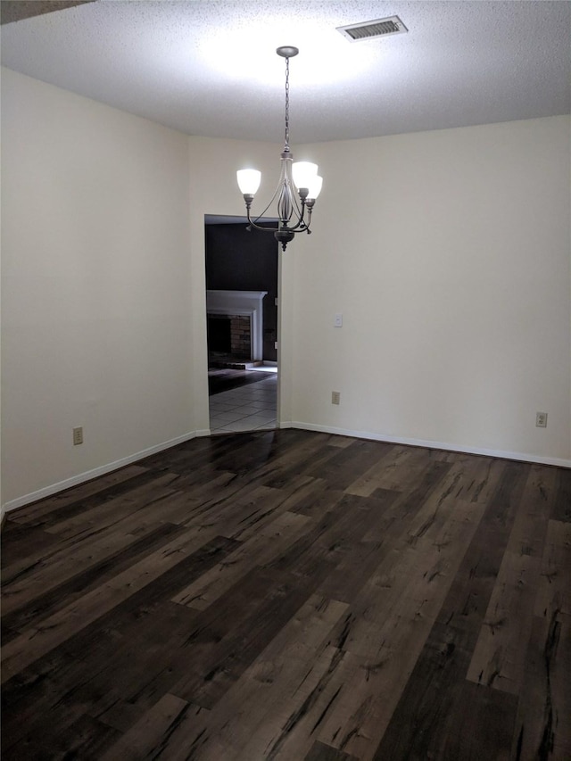 unfurnished dining area featuring a fireplace, a textured ceiling, a chandelier, and dark hardwood / wood-style floors