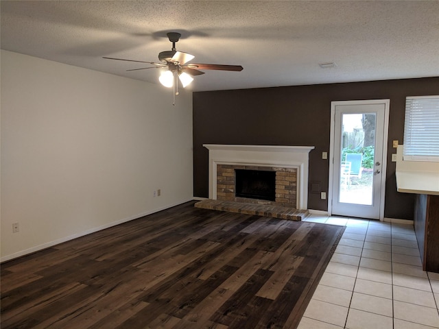 unfurnished living room with ceiling fan, a textured ceiling, light tile patterned floors, and a brick fireplace