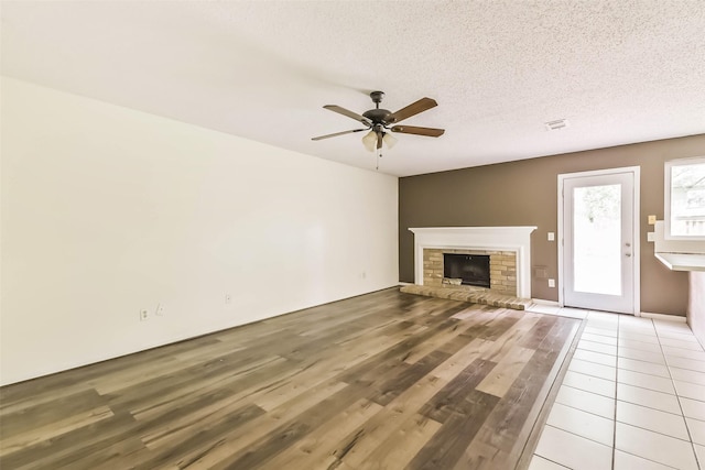 16002 Maple Acres Ct, Houston, TX 77095 - unfurnished living room featuring ceiling fan, a brick fireplace, light wood-style flooring, and a textured ceiling