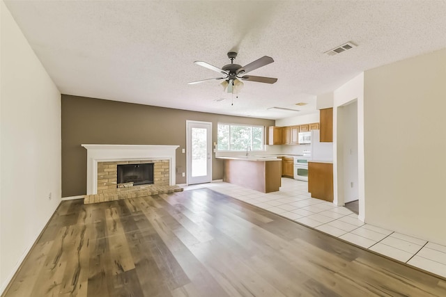 16002 Maple Acres Ct, Houston, TX 77095 - unfurnished living room featuring ceiling fan, light wood-type flooring, a brick fireplace, and a textured ceiling