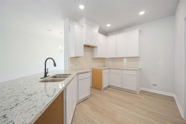 kitchen featuring white cabinets, light stone countertops, light hardwood / wood-style floors, and sink