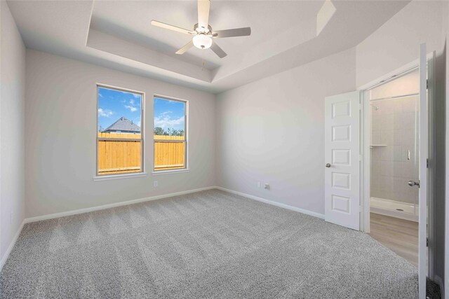 unfurnished room featuring a raised ceiling, light colored carpet, and ceiling fan