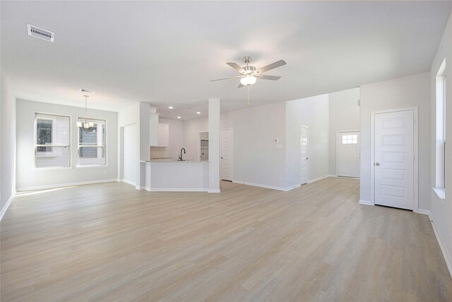 unfurnished living room featuring ceiling fan with notable chandelier, light wood-type flooring, and sink