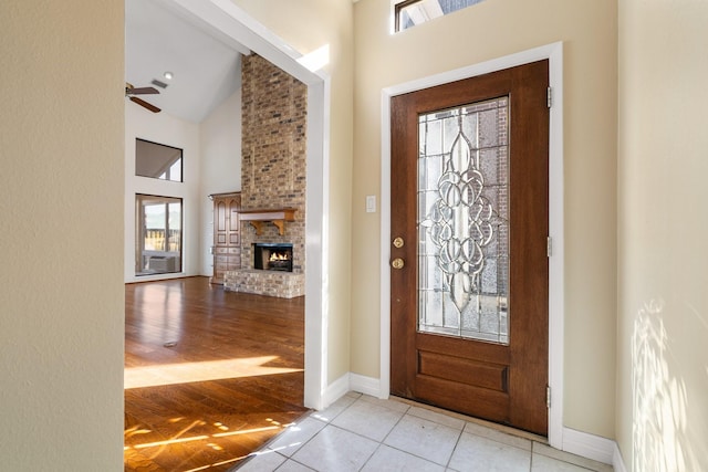 foyer entrance with ceiling fan, a brick fireplace, high vaulted ceiling, and light tile patterned floors