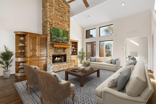 living room with a high ceiling, a brick fireplace, dark wood-type flooring, and ceiling fan