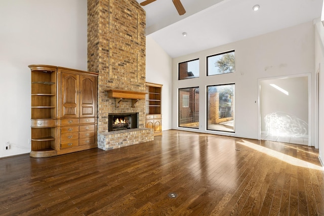 unfurnished living room featuring a high ceiling, dark hardwood / wood-style flooring, a brick fireplace, and ceiling fan