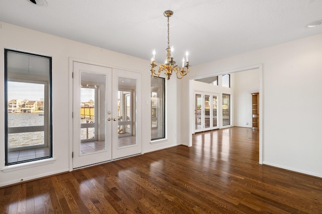 unfurnished dining area with french doors, dark hardwood / wood-style flooring, and a notable chandelier