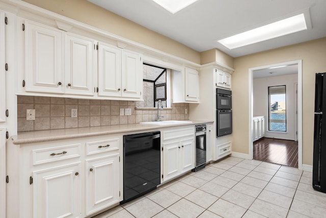 kitchen featuring sink, white cabinets, light tile patterned flooring, backsplash, and black appliances