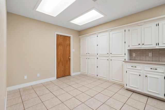 kitchen with light tile patterned floors, white cabinets, and backsplash