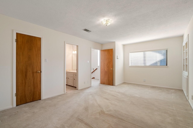 unfurnished bedroom featuring ensuite bathroom, light colored carpet, a closet, and a textured ceiling