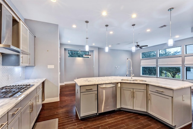 kitchen with light stone counters, wall chimney exhaust hood, appliances with stainless steel finishes, ceiling fan, and sink