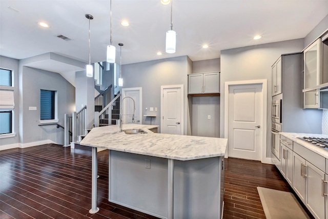 kitchen with a center island with sink, gray cabinetry, hanging light fixtures, a breakfast bar, and sink