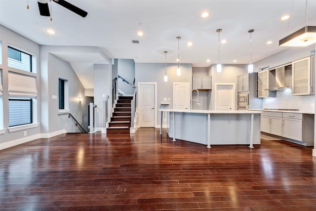 kitchen with a breakfast bar area, an island with sink, pendant lighting, decorative backsplash, and wall chimney range hood