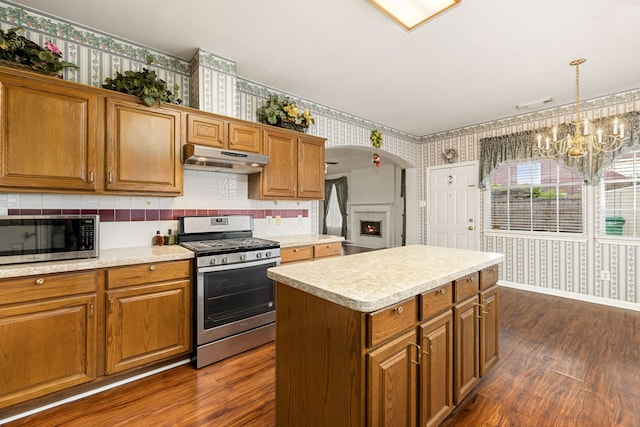 kitchen featuring appliances with stainless steel finishes, a notable chandelier, dark hardwood / wood-style flooring, a kitchen island, and decorative light fixtures