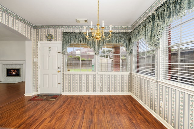 unfurnished dining area with wood-type flooring, a fireplace, a chandelier, and a wealth of natural light