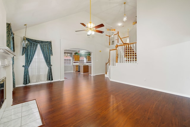 unfurnished living room with ceiling fan with notable chandelier, high vaulted ceiling, a fireplace, and hardwood / wood-style floors