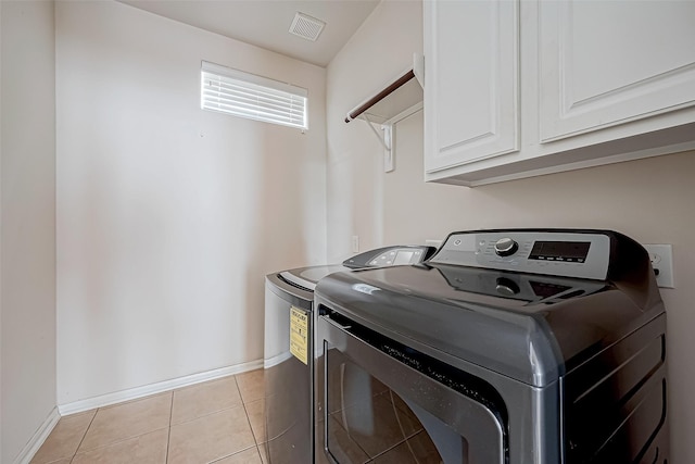 clothes washing area featuring washing machine and clothes dryer, light tile patterned floors, and cabinets