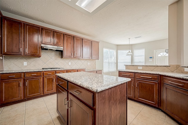 kitchen with decorative light fixtures, tasteful backsplash, a kitchen island, stainless steel gas stovetop, and light tile patterned flooring