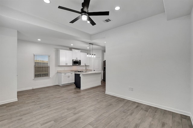 kitchen featuring a kitchen island with sink, light hardwood / wood-style floors, hanging light fixtures, ceiling fan, and white cabinets