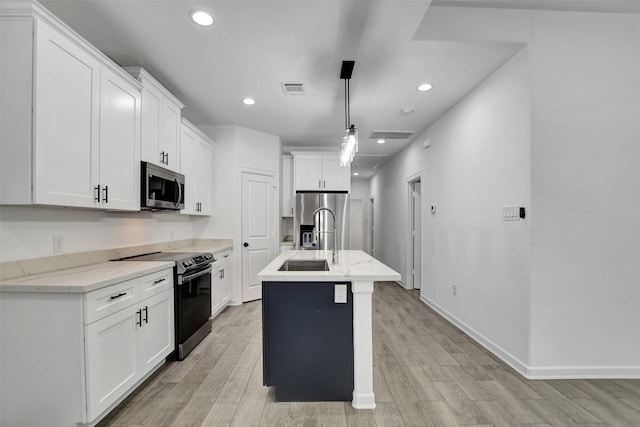 kitchen featuring light hardwood / wood-style flooring, hanging light fixtures, a center island with sink, white cabinets, and appliances with stainless steel finishes