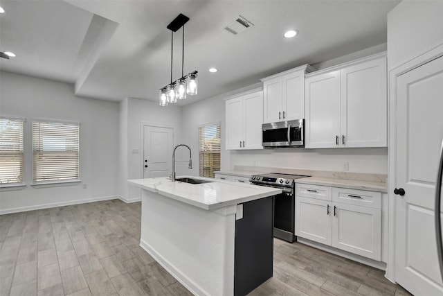 kitchen featuring stainless steel appliances, sink, white cabinets, hanging light fixtures, and a kitchen island with sink